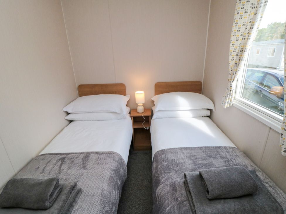 A bedroom with two single beds and a nightstand with a lamp at 14 Pines in Cayton Bay