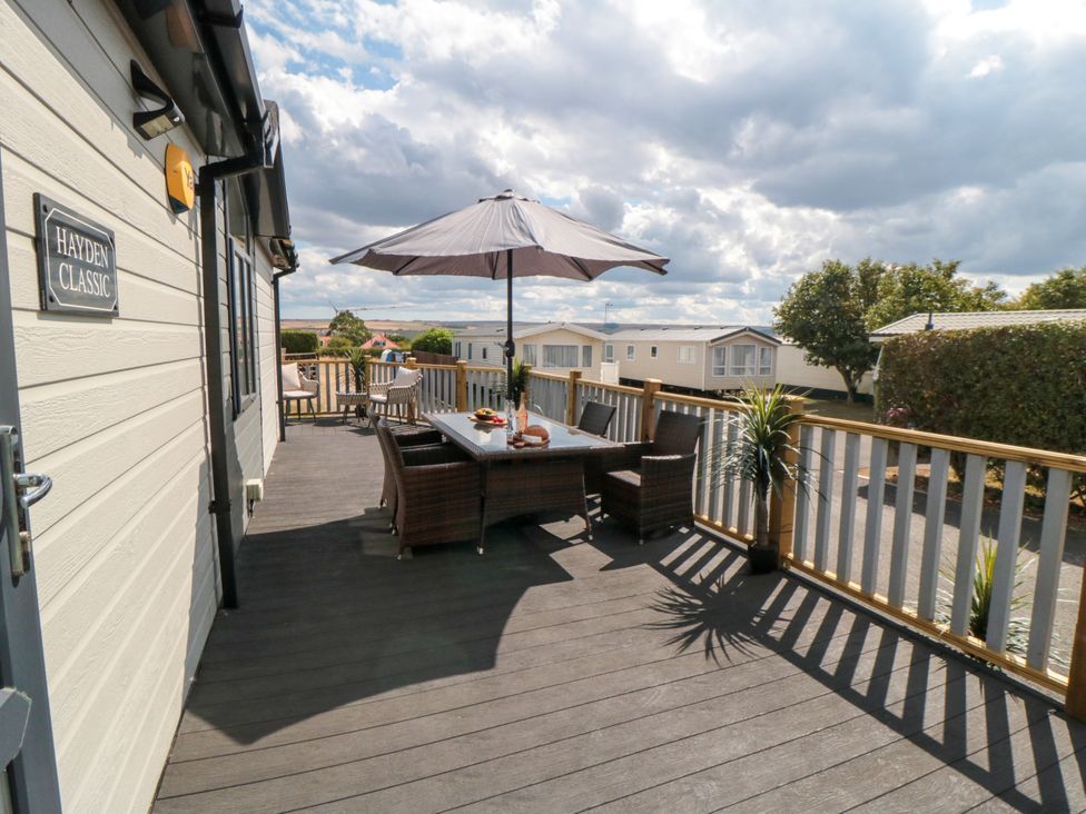 An outdoor terrace with a table and chairs at Sea Glass Lodge in Runswick Bay