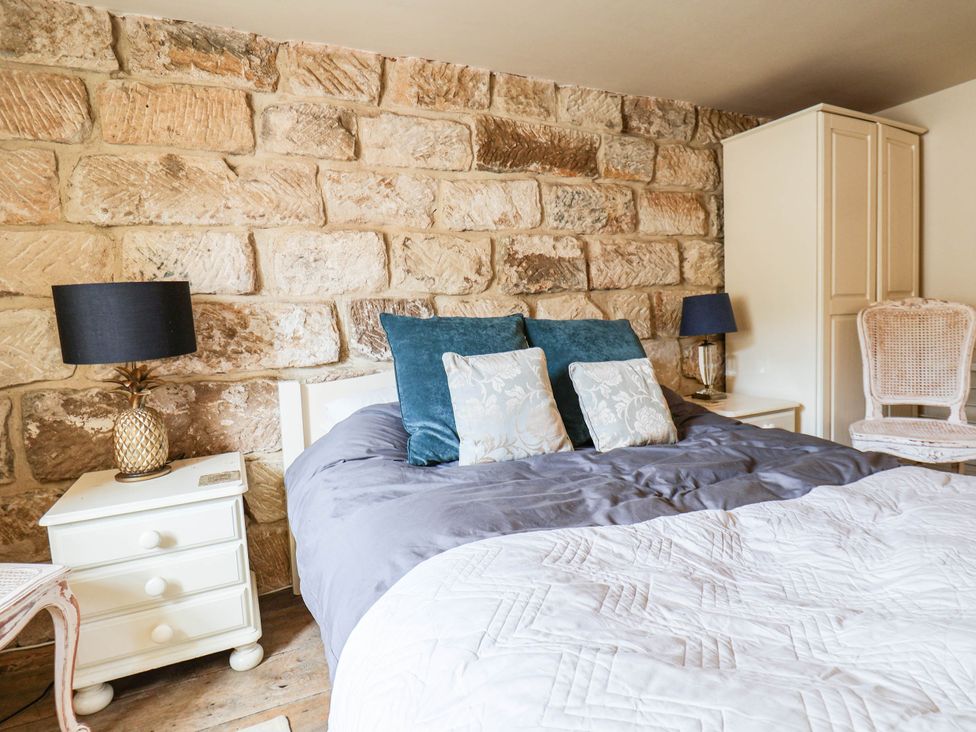 A bedroom with a stone wall, bed, lamp, and wardrobe at bellebeck