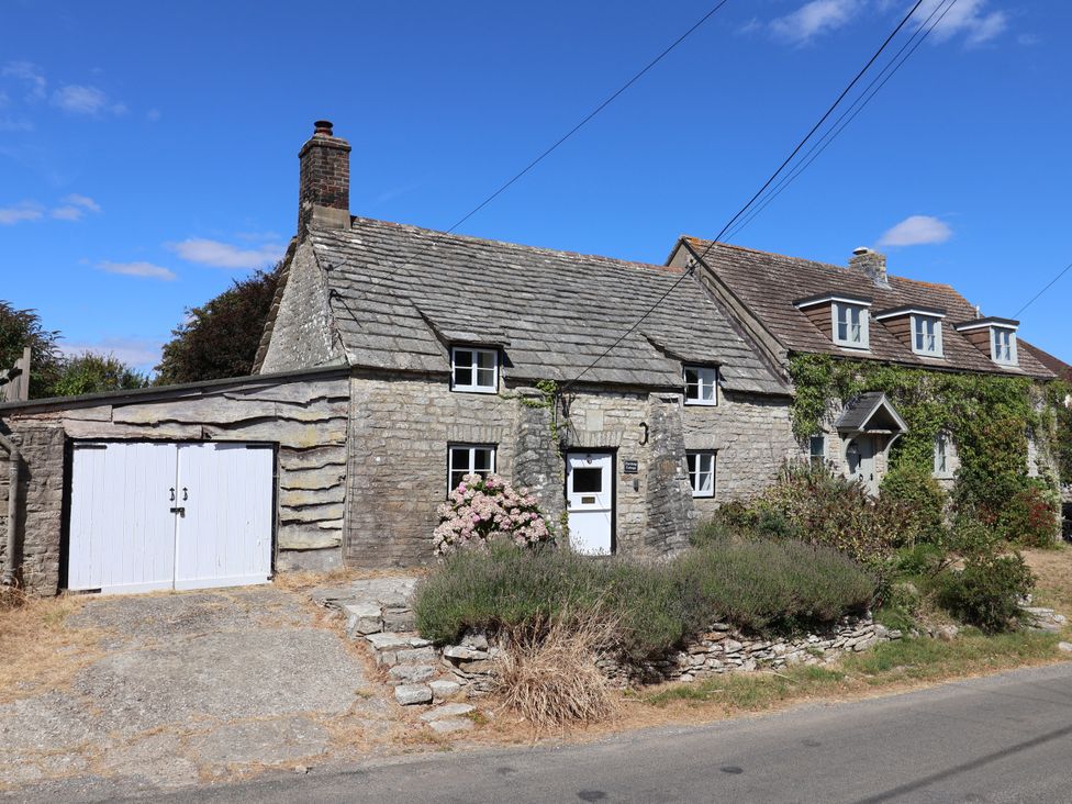 A cottage with a garage and flower beds at Farthing Cottage Corfe Castle