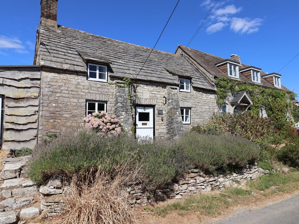 A cottage with stone walls and flowers outside at Farthing Cottage in Corfe Castle