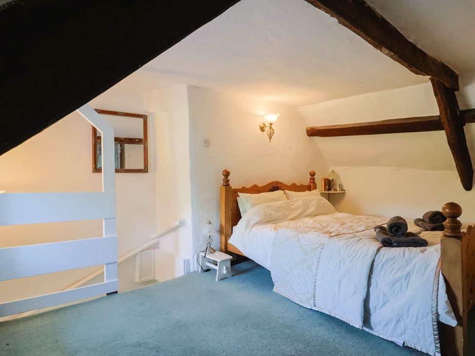 A bedroom with a bed and towels on a shelf at Farthing Cottage in Corfe Castle