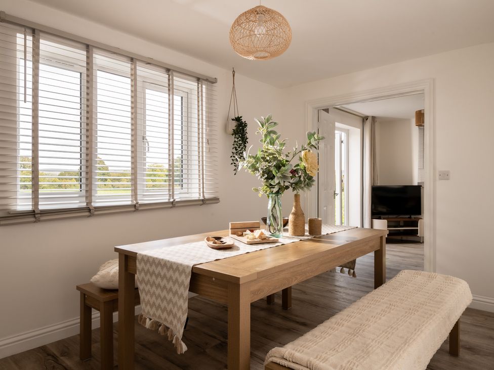 A dining room with a table, bench, and windows at Hambledon Hill Cottage in Blandford Forum