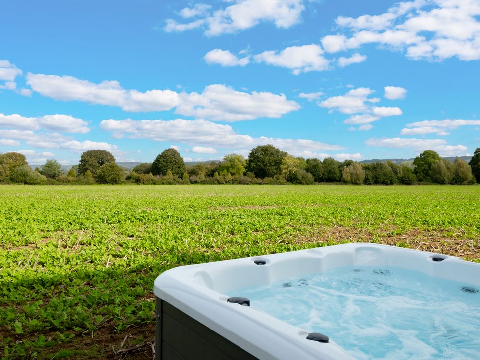 A hot tub in a grassy area with trees and clouds at Hambledon Hill Cottage in Blandford Forum