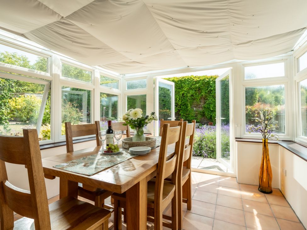 A dining table with chairs and flowers in a conservatory at Charming Countryside Cottage in Blandford Forum