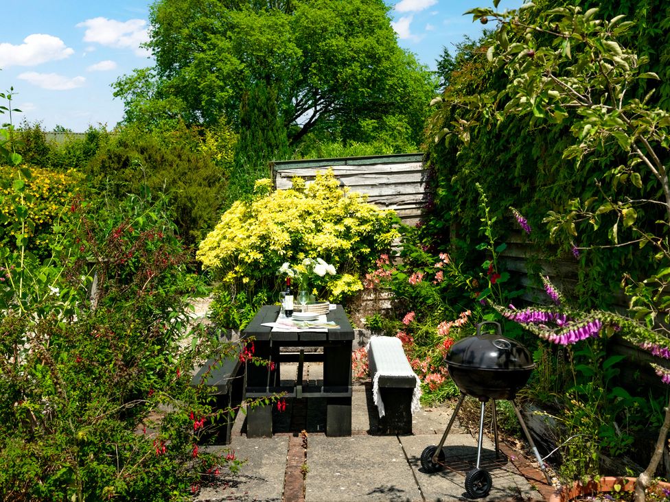A garden with a table, chairs, and a barbecue grill at Charming Countryside Cottage, Blandford Forum