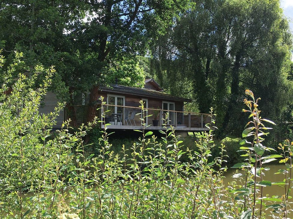 A wooden house with a deck by a river surrounded by trees and plants at 1 Water's Edge