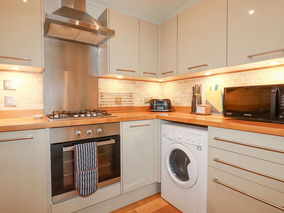 A kitchen with cabinets, cooker, washing machine and microwave at 1 Water's Edge