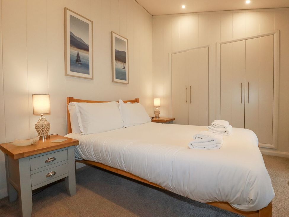 A bedroom with a bed, bedside table, lamp, and wardrobe at 1 Water's Edge