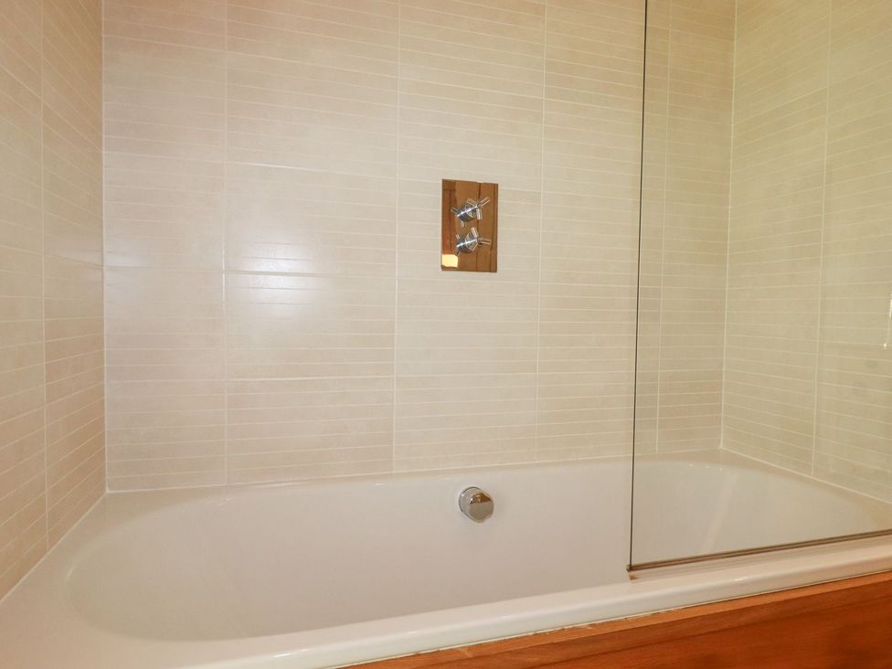 A bathtub with a shower above and a glass panel at 1 Water's Edge