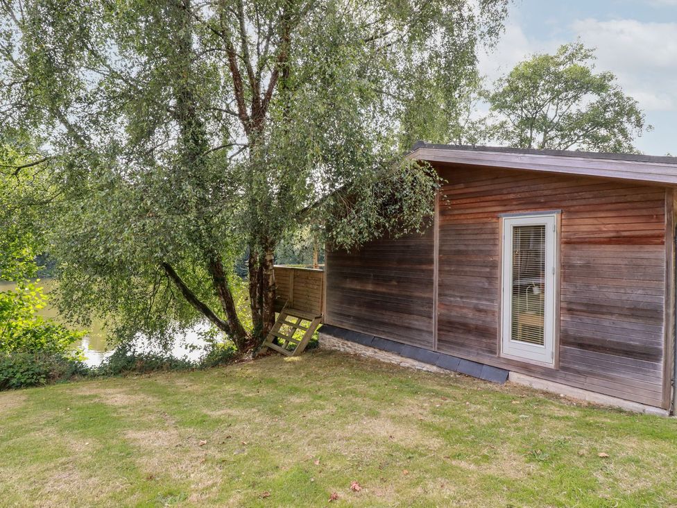 An outdoor area with a wooden cabin, tree, and grass by a water at 1 Water's Edge