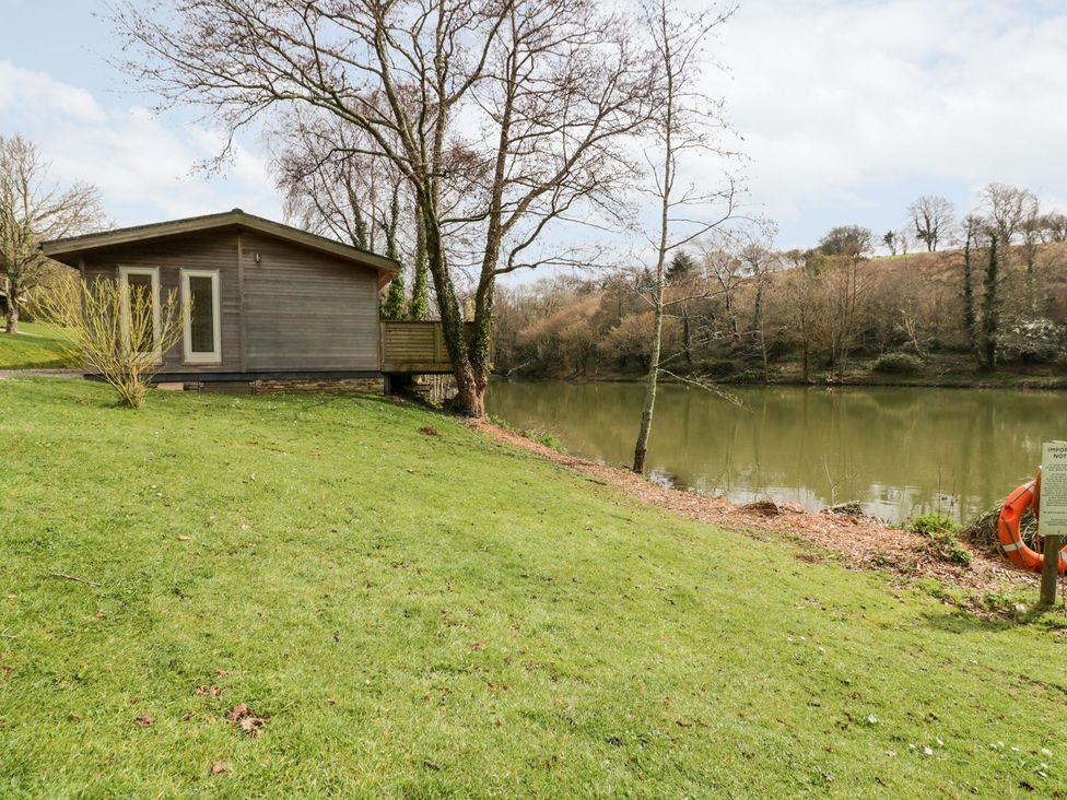 A wooden cabin next to a lake with grass and trees at 1 Water's Edge