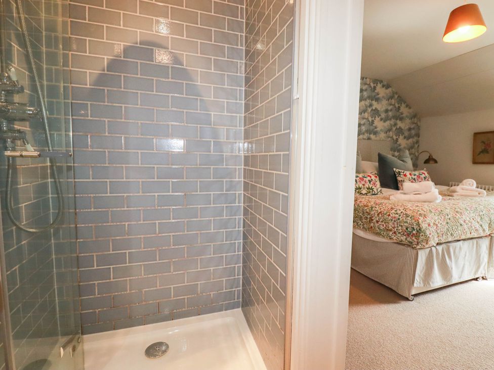 A shower with glass door and adjoining bedroom with floral bedding at The Homestead