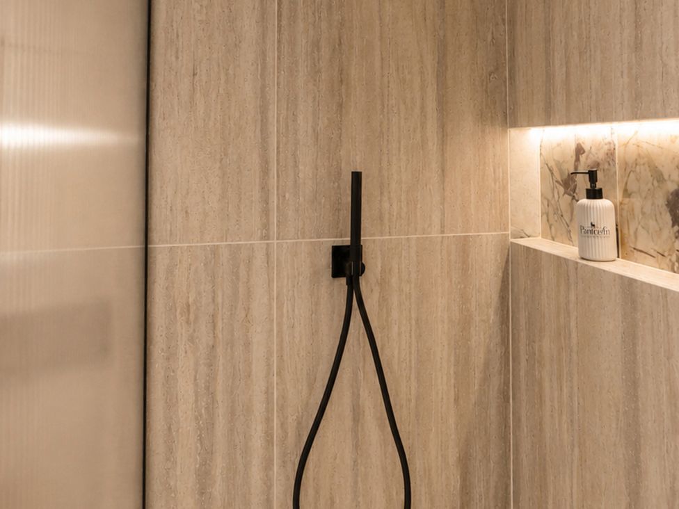 A shower area with tiled walls and a soap dispenser at The Hog Hut in Llanarth