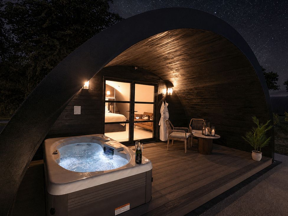 An outdoor area with a hot tub, chairs and a table at The Hog Hut in Llanarth