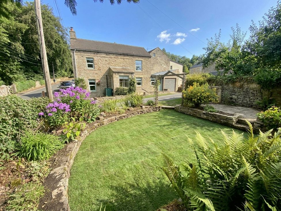 A garden with flowers and a house visible at Woody Bank in Middleton-In-Teesdale