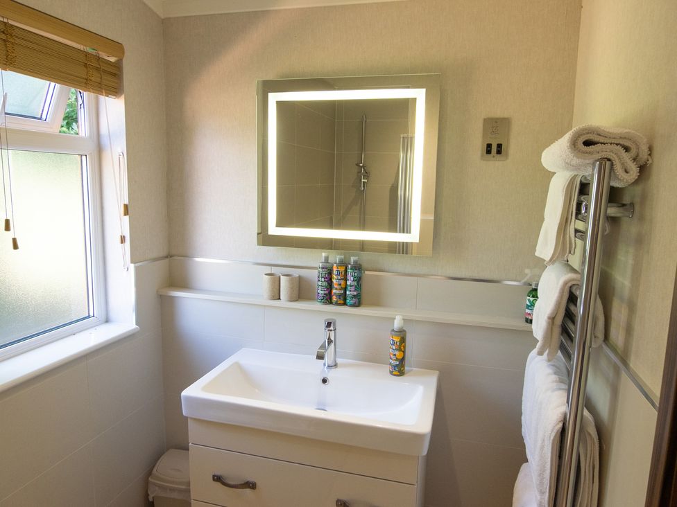 A bathroom with a sink, mirror, and towels at Ash Lodge in Stowmarket