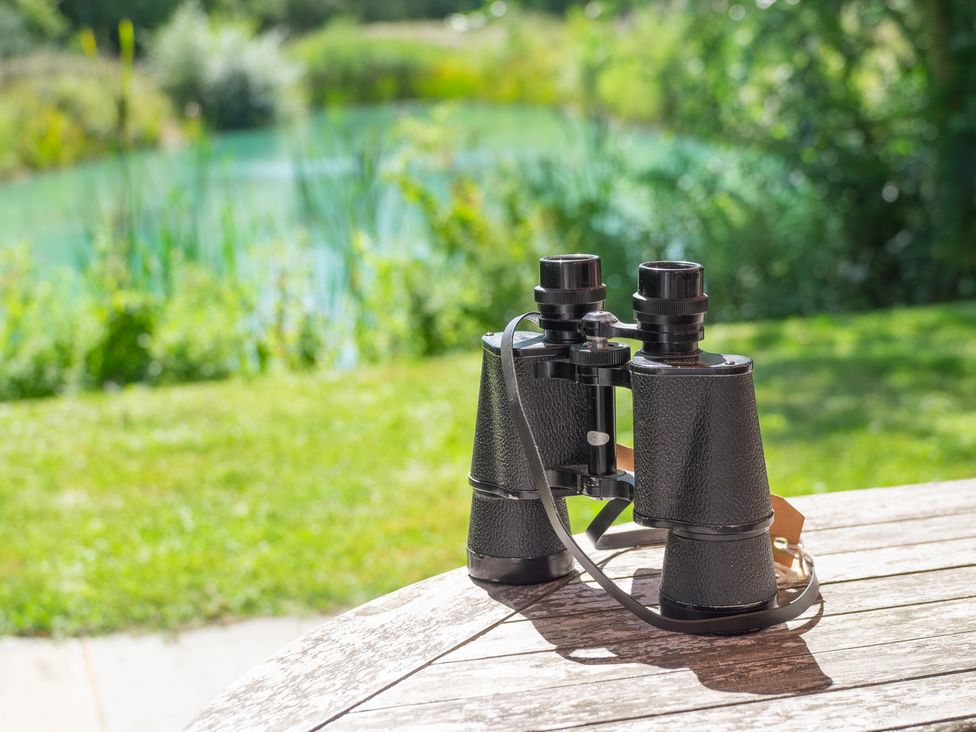 Binoculars on a wooden table near a lake at Ash Lodge in Stowmarket
