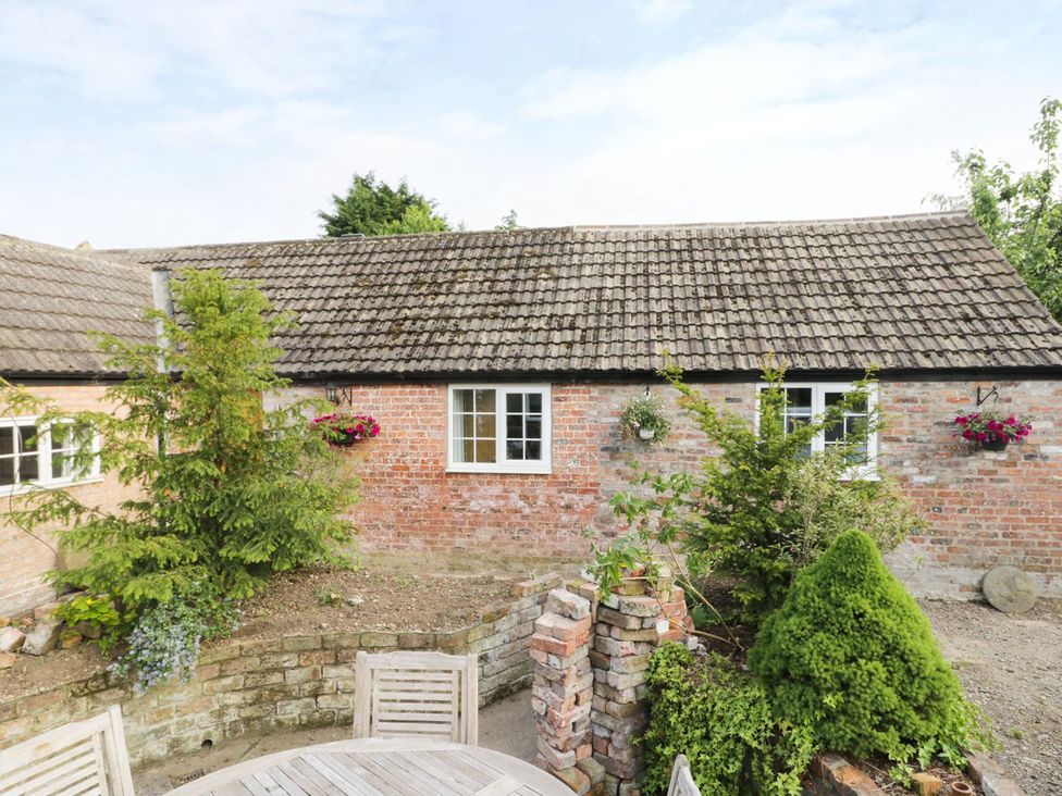 A garden with a brick wall and windows at Millstone Cottage Beverley