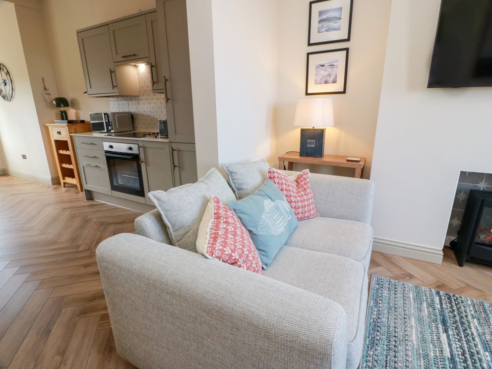 A living room with a sofa and kitchen area at Sandy Toes in Powfoot, Annan