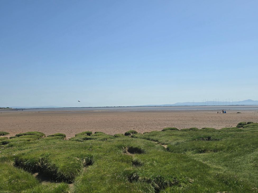 A beach with grass and people sitting at the water edge at Sandy Toes in Powfoot, Annan