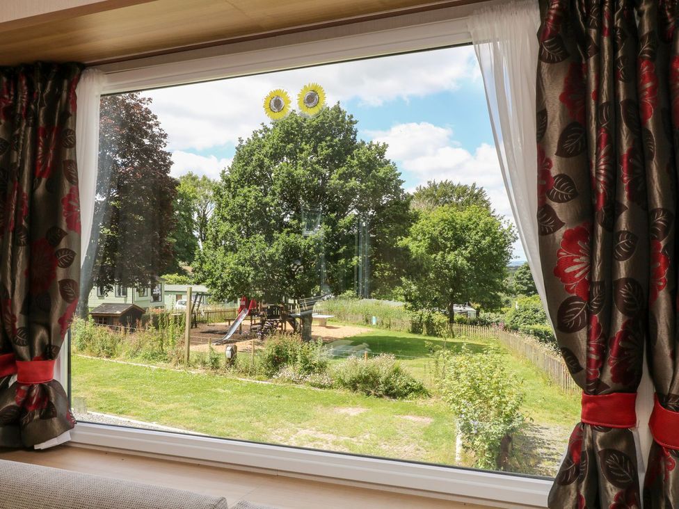 A window with curtains overlooking a garden and playground at Fur Tor in Tavistock