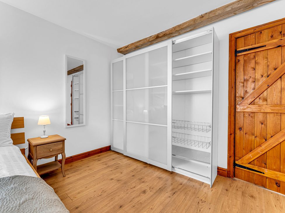 A bedroom with a bed, bedside table, mirror, and wardrobe at Oxhay Barn Newcastle