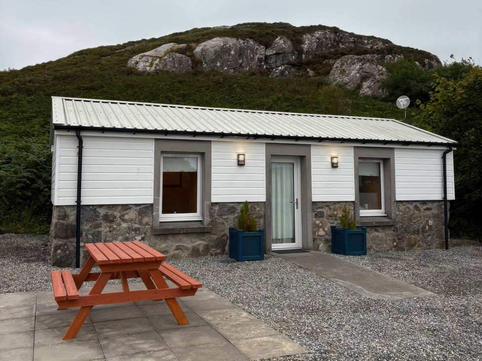 A house with a picnic table and greenery at Bothan Beag, Daliburgh, Isle Of South Uist
