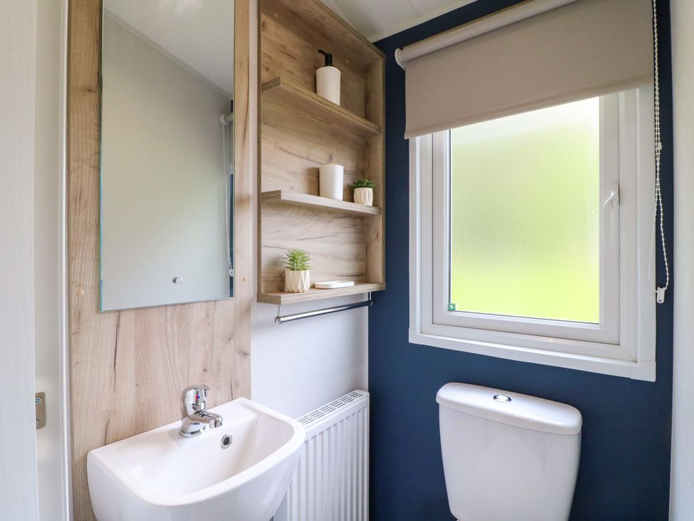 A bathroom with a sink, toilet, and shelf at Barn Owl Lodge in Coalville