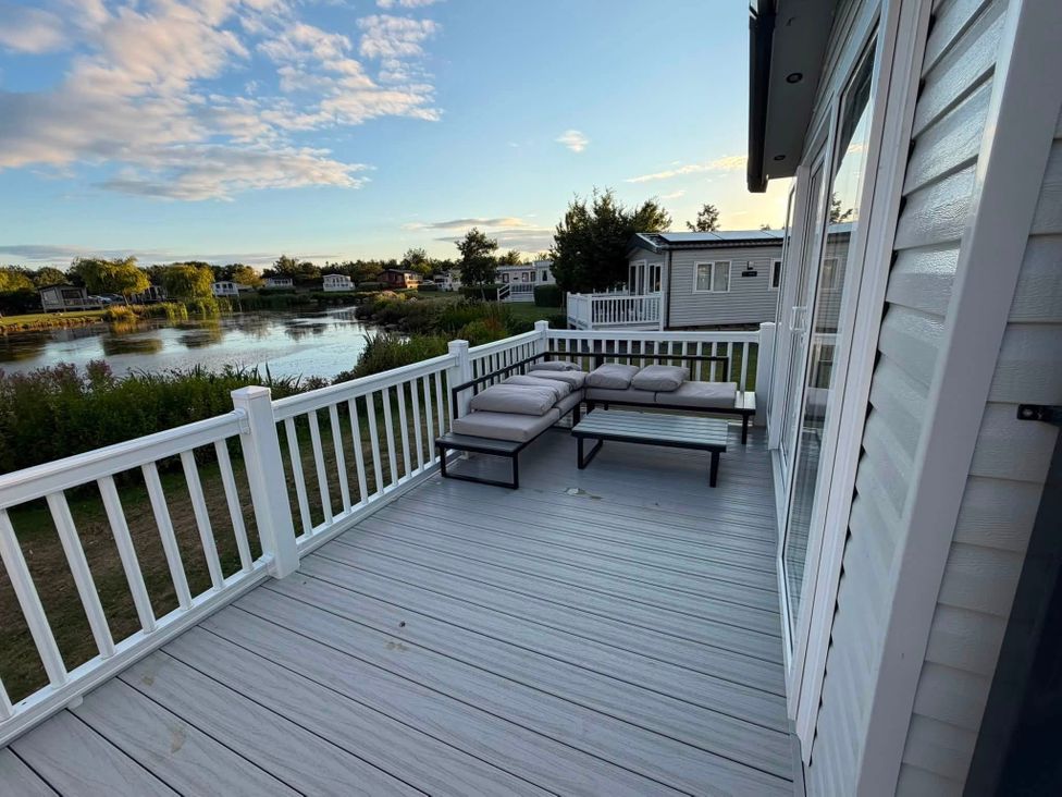 A deck with a sofa and coffee table overlooking a water view at Haggerston Castle - Lakeside Retreat, Berwick-upon-Tweed