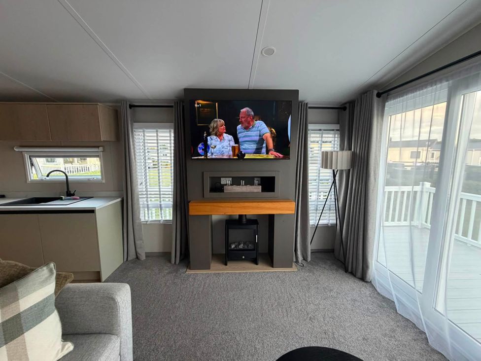 A living room with a television on the wall and a sofa at Haggerston Castle - Lakeside Retreat in Berwick-upon-Tweed