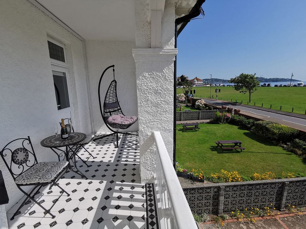 A balcony with a hanging chair and table overlooking a garden and sea at Russell House in Paignton