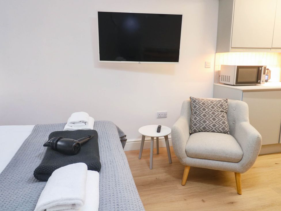 A bedroom with a television, armchair, and kitchenette at The Cabin in St Ives