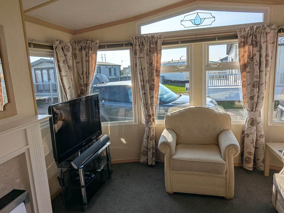 A living room with a television and windows at Beachcomber Cabin Dog Friendly Anderby Creek in Lincolnshire