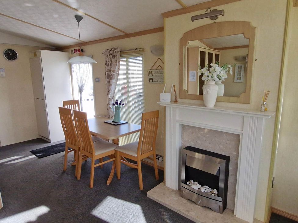 A dining room with a table, chairs, and a fireplace at Beachcomber Cabin Dog Friendly Anderby Creek in Lincolnshire
