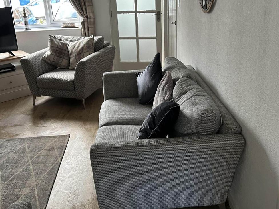 A living room with a sofa, armchair, and television and door at the property