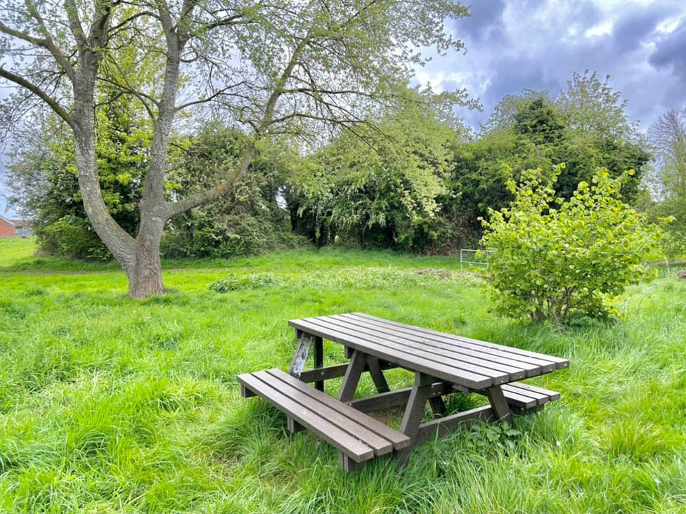 A wooden table and benches in a garden with grass and trees at 