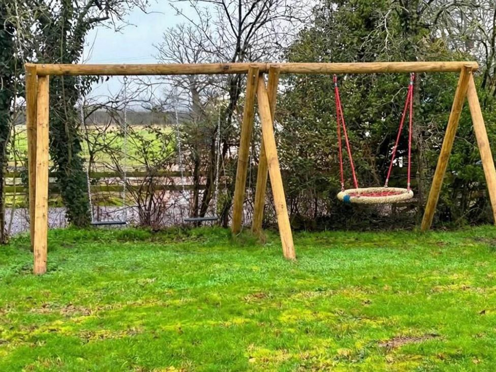 A swing set with a hanging platform and swings in a yard