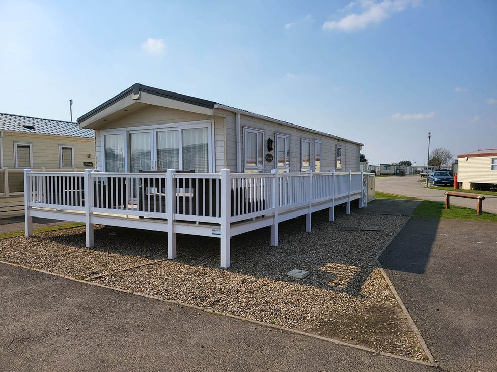 A mobile home with wooden decking and gravel outside at a holiday park