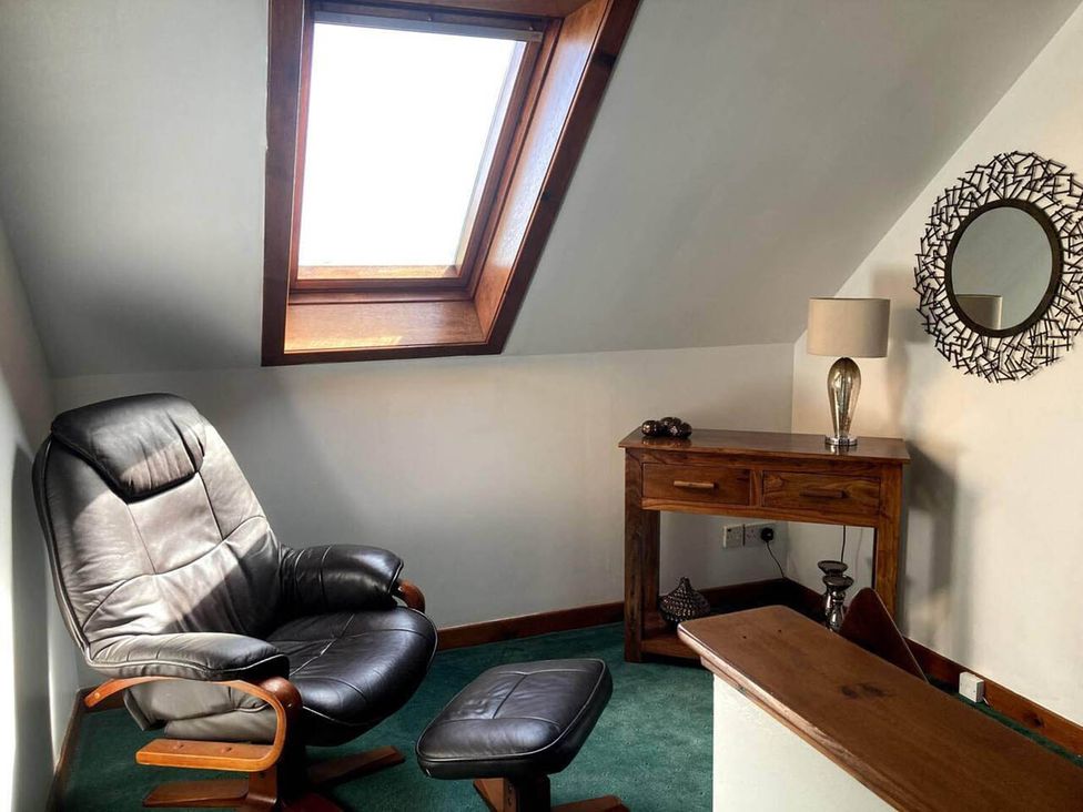 A chair and table with a lamp under a skylight in an attic