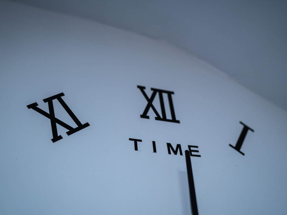 A clock with Roman numerals and the word TIME on a wall