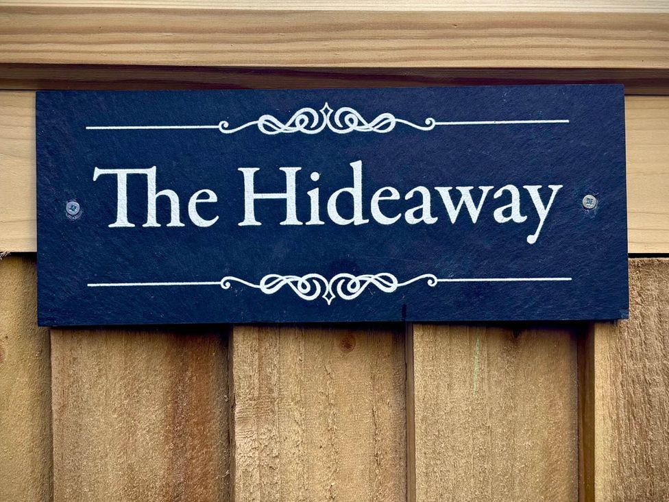 A sign that reads The Hideaway mounted on a wooden fence