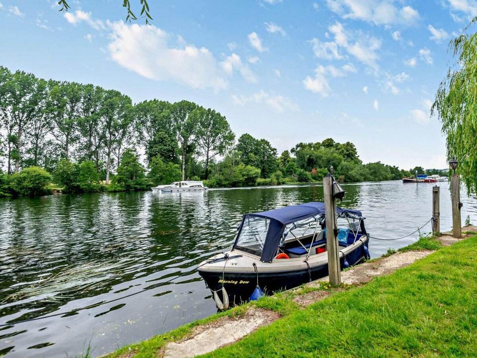 A boat tied at a dock on a river with trees in the background at Luxurious 5 Bedroom House in Cookham near Marlow
