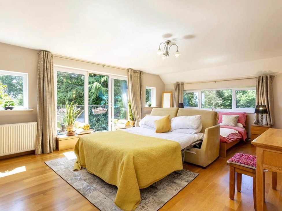 A bedroom with a bed, bedside table, and large windows at Sleeps 10 to 18 Parking Garden Pool Hot Tub Balcony in Friston