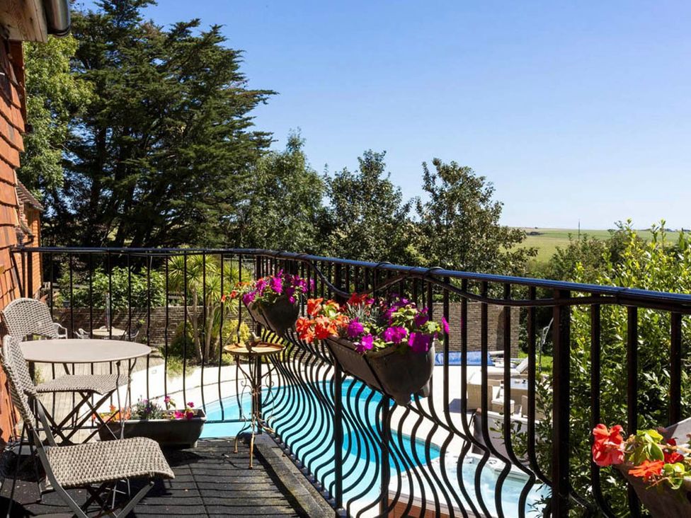 A balcony with a table and chairs overlooking a swimming pool at Sleeps 10 to 18 Parking Garden Pool Hot Tub Balcony in Friston
