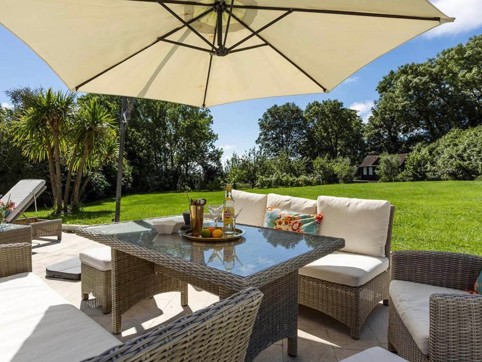 A garden area featuring a table and chairs under an umbrella at Sleeps 10 to 18 Parking Garden Pool Hot Tub Balcony in Friston
