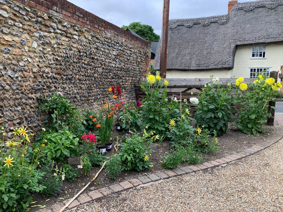 A garden with flowers near a stone wall and a thatched roof house at the property location