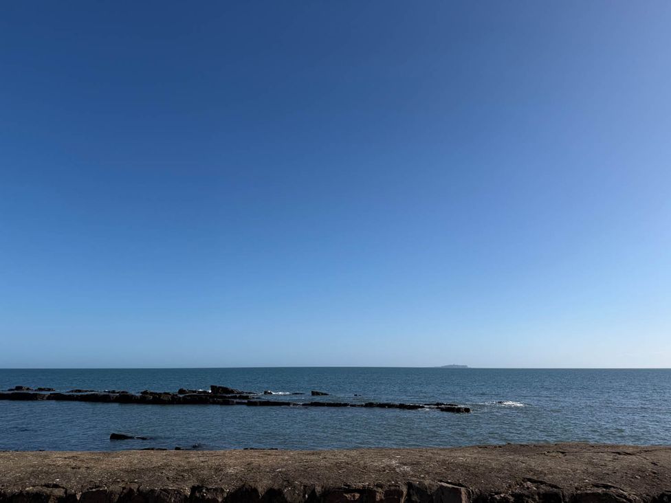 A view of the ocean with rocks in the foreground and clear sky at a beach