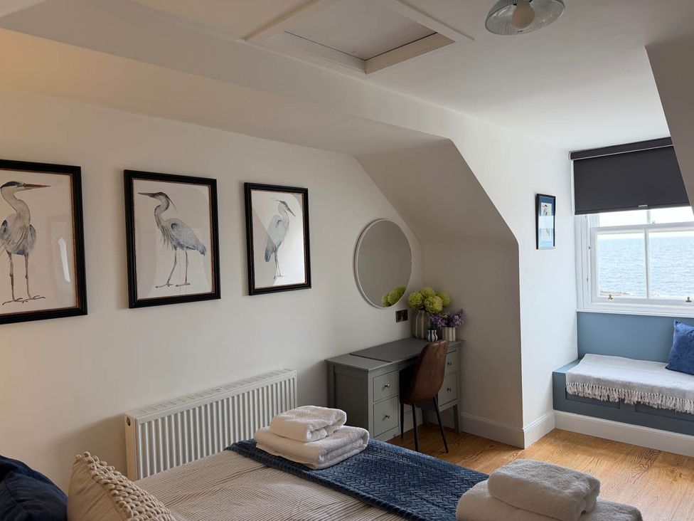 A bedroom with a bed, desk, and window showing water view at 