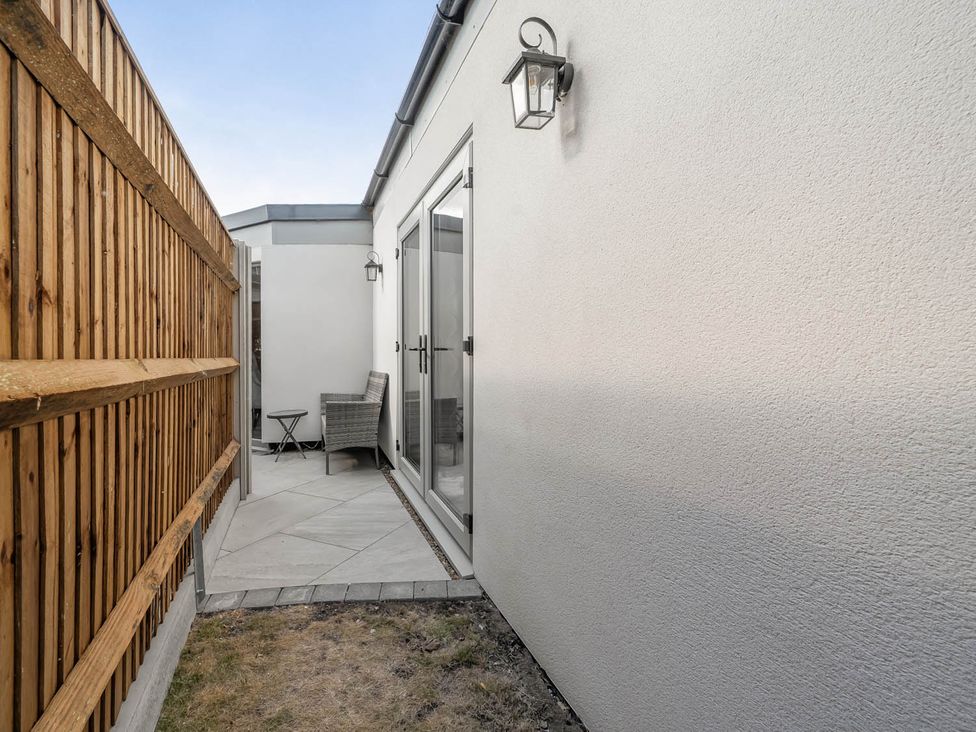 An outdoor area with a chair and table near a wall at Annexe Bungalow Sleeps 2 Maximum Parking Garden in Scratby